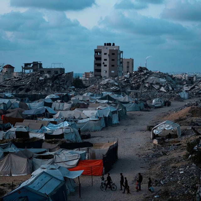 Palästinenser, die durch die israelische Luft- und Bodenoffensive auf den Gazastreifen vertrieben wurden, gehen in der Abenddämmerung über einen Platz in einem behelfsmäßigen Zeltlager.