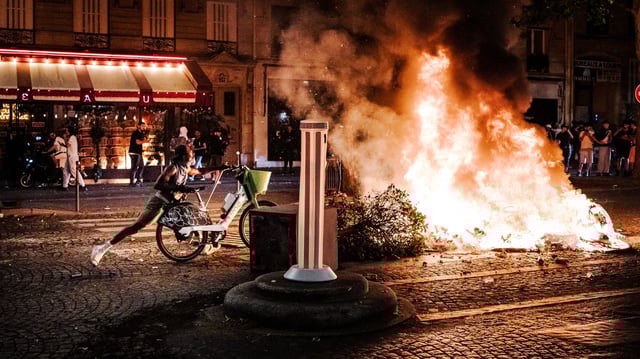 Un homme pousse un vélo dans un feu allumé au milieu d’une rue, près des Champs-Élysées, lors des violences urbaines survenues en marge des célébrations de la victoire du PSG en finale de la Ligue des champions, samedi soir, à Paris.