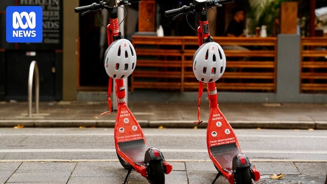Two orange e-scooters in the Perth CBD on a footpath.