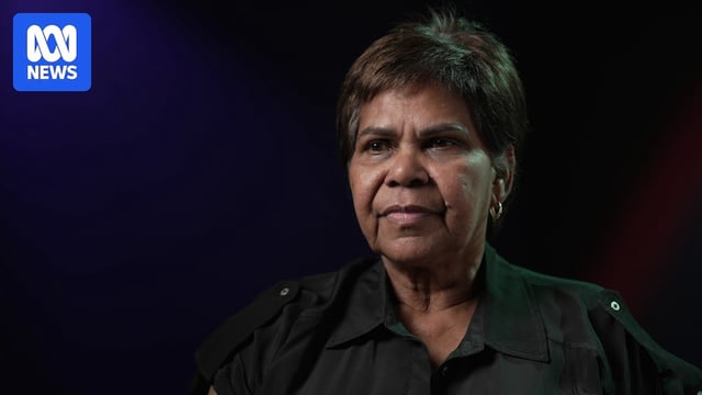 A woman sits in front of a dark backdrop