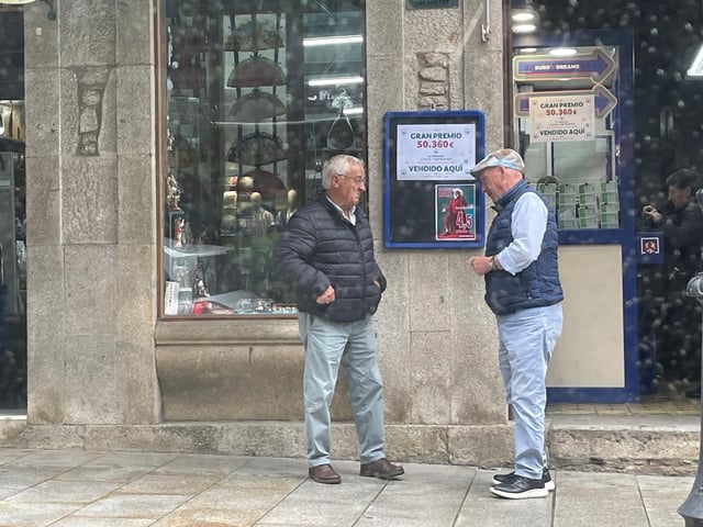Dos vecinos observan el cartel del premio delante de la administración de la calle Principal.