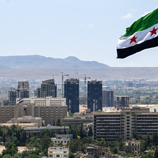 A large Syrian flag flutters above Tishreen Park in Damascus on June 4, 2025. Syria's interim President Ahmed al-Sharaa has in six months established himself internationally and had crippling sanctions removed, but still needs to rebuild national institutions, revive the economy and unite the fractured country. (Photo by LOUAI BESHARA / AFP) (Photo by LOUAI BESHARA/AFP via Getty Images)