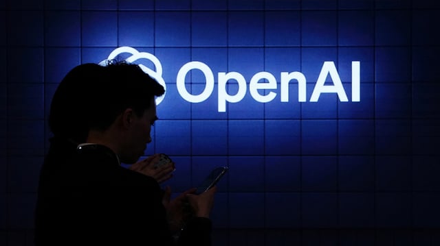 Zwei Menschen in einem dunklen Raum vor einem neonfarbigen OpenAI-Logo.