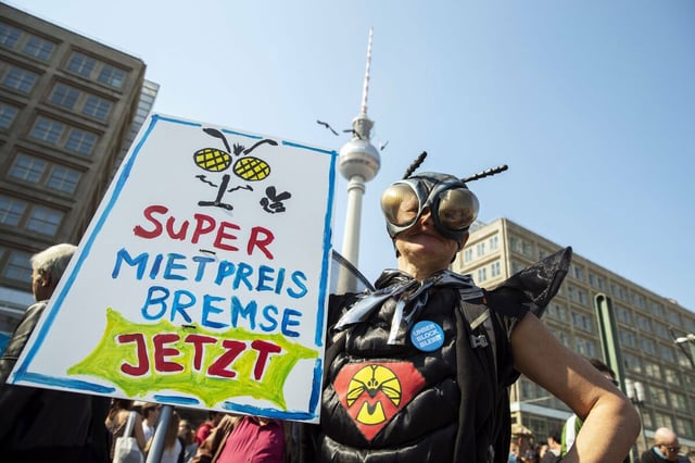 Ein Mensch in einem Kostüm fordert auf einem Plakat "Super Mietpreisbremse jetzt"