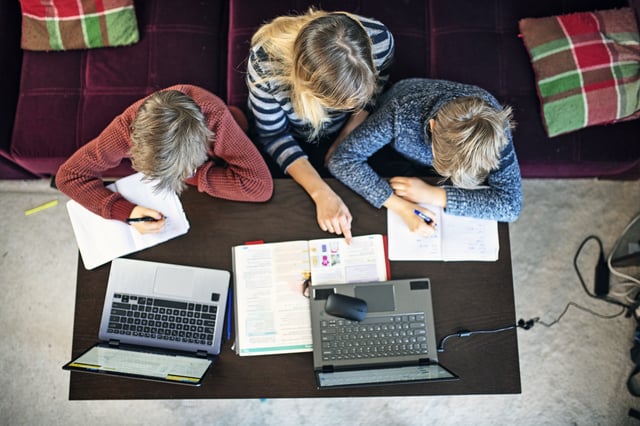 Mother helping sons with homeschooling at home during COVID-19 pandemic.