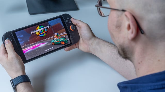 Ein Mann hält eine Nintendo Switch 2 in beiden Händen. Auf dem Bildschirm ist das Spiel „Mario Kart World“ mit Luigi zu sehen.