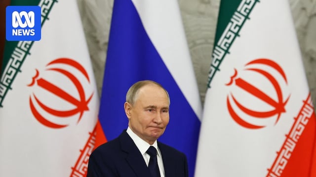 Russian President Vladimir Putin stands in front of two iranian flags and a russian flag