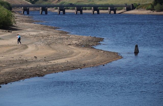 A woman walks along a dry section of the bed of the Baitings reservoir after a prolonged period without rain, which resulted in water levels dropping, near Ripponden, Britain, May 13, 2025. REUTERS/Phil Noble/ File Photo