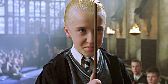 Draco grinning about to duel with his wand in front of his face