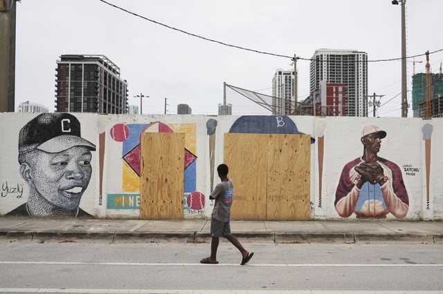 A person walks past murals of baseball legends Minnie Miñoso, second from left, and Jackie Robinson, second from right, covered with plywood after being defaced in Miami's Overtown neighborhood, Thursday, June 5, 2025, in Miami. (AP Photo/Lynne Sladky)