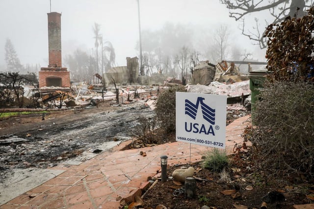 A sign from USAA can be seen in front of the remains of a home in the Pacific Palisades neighborhood of Los Angeles on Feb. 2. USAA, the sixth largest home insurer in California as of 2023, has been accused of underinsuring three families in Pacific Palisades and one in Altadena.
