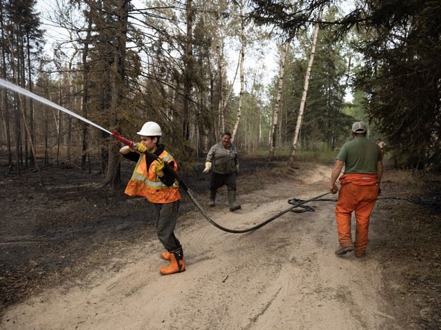 Local fire crews from the hamlet of Weyakwin  water down scorched earth on Saturday, May 31, 2025.
