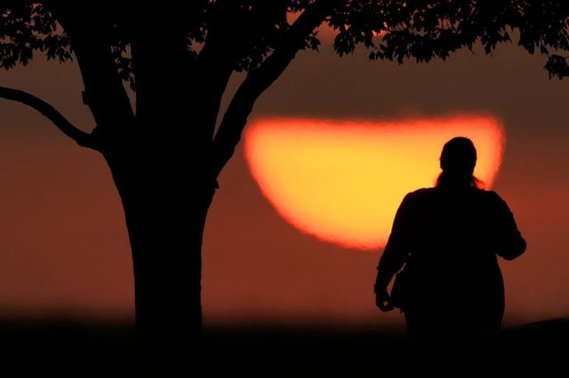 FILE - A woman watches the sun set on a hot day, Aug. 20, 2023, in Kansas City, Mo. 