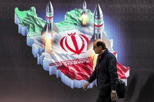 A man walks past a banner depicting missiles launching from a representation of the map of Iran coloured with the Iranian flag in central Tehran on April 15, 2024. Iran on April 14 urged Israel not to retaliate militarily to an unprecedented attack overnight, which Tehran presented as a justified response to a deadly strike on its consulate building in Damascus.