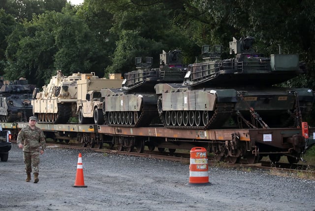 This 2019 photo shows two M1-A1 Abrams tanks and other military vehicles sit on guarded rail cars at a rail yard in Washington, DC.