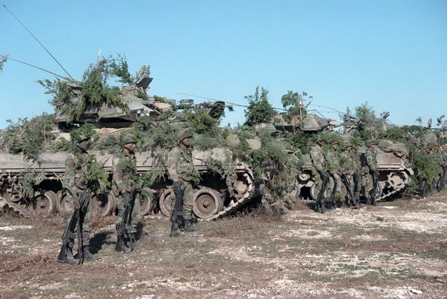 Soldiers stand beside their camouflaged M2 Bradley Fighting Vehicles at the Shell Point training area in Fort Hood, Texas, in 1986.