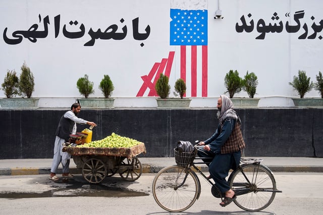 A cyclist passes in front of the former US embassy while a vendor waits for customers, in Kabul, Afghanistan, on June 5.