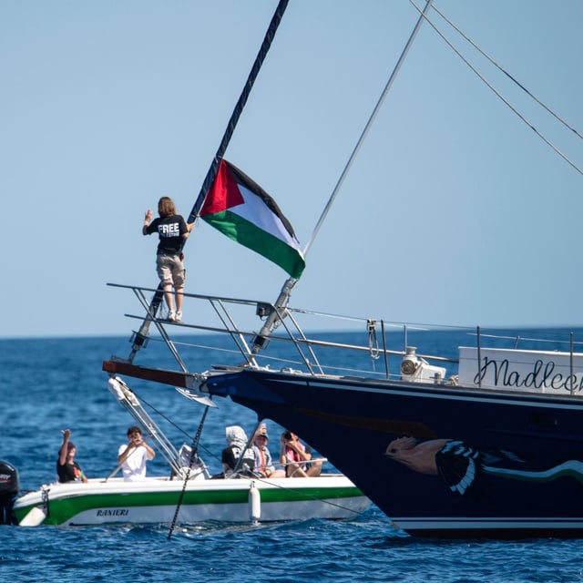 Climate activist Greta Thunberg stands near a Palestinian flag after boarding the Madleen boat and before setting sail for Gaza along with activists of the Freedom Flotilla Coalition, departing from the Sicilian port of Catania, Italy, Sunday, June 1, 2025. (AP Photo/Salvatore Cavalli)