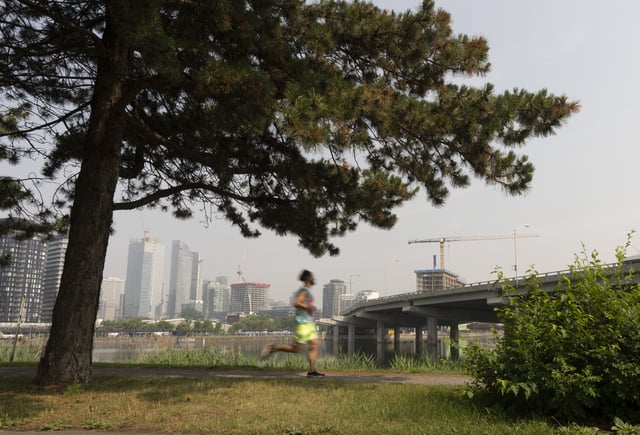 A man jogs beside the Peel Basin on Friday, June 30, 2023 in downtown Montreal. Environment Canada says forest fires are causing poor air quality today across much of Quebec and Ontario. THE CANADIAN PRESS/Christinne Muschi
