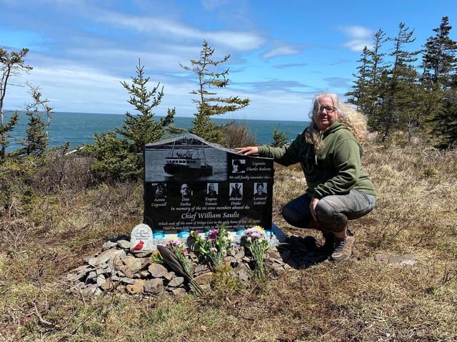 Lori Cogswell-Phillips crouches alongside a monument on Tuesday, May 10, 2022 in Delap's Cove, N.S. remembering her son Aaron Phillips and other members of the crew of the Chief William Saulis. She and a group of friends installed it near the site of where the boat sank on Dec. 15, 2020. THE CANADIAN PRESS/Lori Cogswell-Phillips