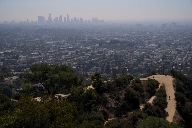 FILE - A person with a dog walks along a trail as a layer of smog blankets downtown Los Angeles, Tuesday, Oct. 1, 2024. (AP Photo/Jae C. Hong, File)