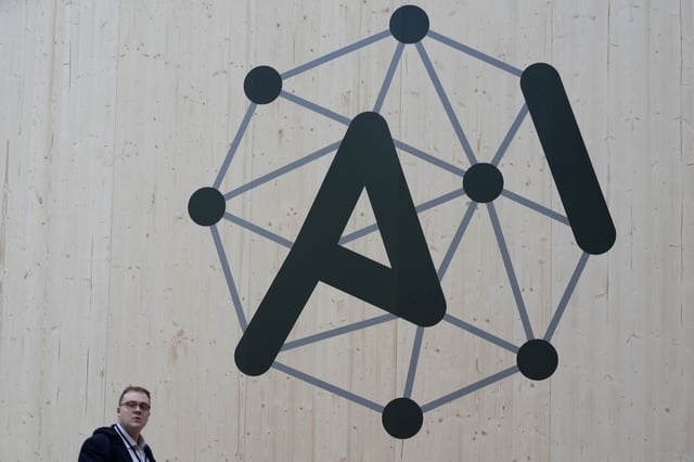 An attendee walks by a wall with a logo during an Artificial Intelligence Action Summit at the Grand Palais in Paris, Monday, Feb. 10, 2025. (AP Photo/Michel Euler)