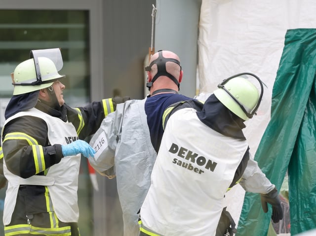Einsatzkräfte helfen einem Kollegen aus seiner Schutzkleidung neben einem Dekontaminationszelt auf dem Gelände eines DHL-Verteilerzentrums in Langenzenn bei Nürnberg.