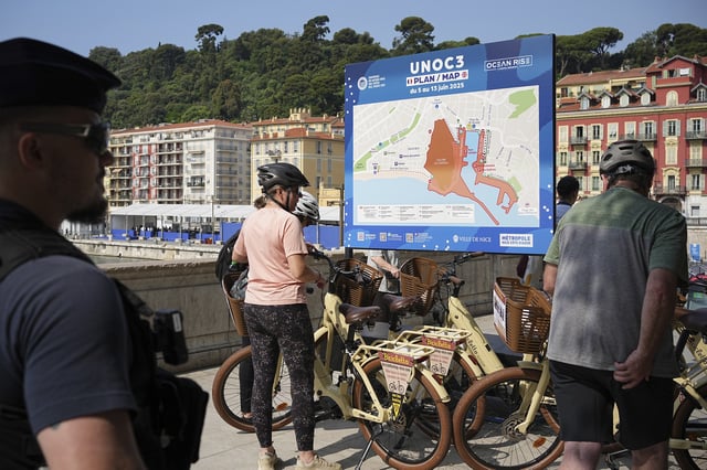 A police officer watches riders by a map of the UN Ocean Conference, Saturday, June 7, 2025 in Nice, French Riviera. (AP Photo/Laurent Cipriani)
