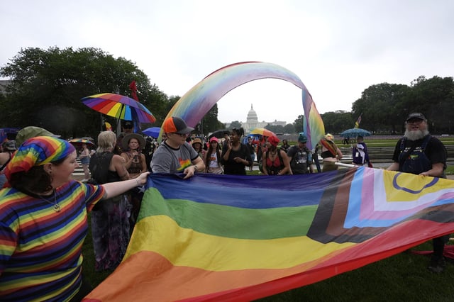 People roll up a wet flag during the World Pride Rally and March with the U.S. Capitol building in the background, Sunday, June 8, 2025, on the National Mall in Washington.