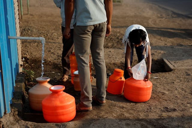 A girl covers a pot filled with water with a plastic sheet to protect it from dust next to a water ATM machine in Solapur, India, March 3, 2025. REUTERS/Francis Mascarenhas