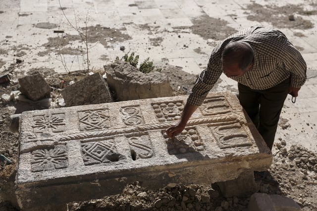 A guard inspects an engraved stone, originally found at a Byzantine underground tomb complex believed to be over 1,500 years old and uncovered by a contractor during the reconstruction of a war-damaged house and brought to a museum yard in Maarat al-Numan, Syria, Friday, May 30, 2025. (AP Photo/Omar Albam)
