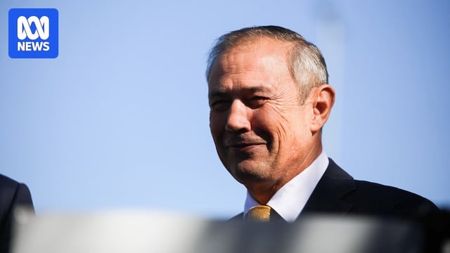 A side profile view of Roger Cook who is smiling while wearing a suit