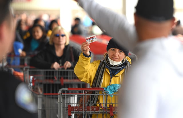 A woman displays her Costco card in order to enter after waiting in a line that snaked around a Costco store in Novato, California on March 14, 2020.