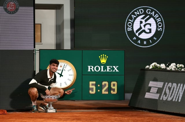 Carlos Alcaraz pose avec le trophée de Roland-Garros devant l'horloge indiquant la durée (5h29) de la finale contre Jannik Sinner, la plus longue de l'histoire du tournoi, le 8 juin 2025 à Paris