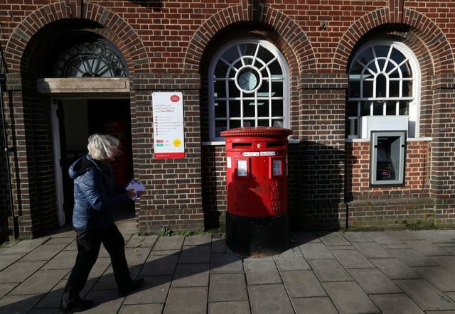 A woman carries mail before posting it outside a branch of Post Office in Swindon, western England, in January 2024