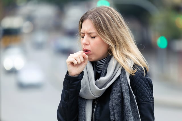 A stock image of a woman coughing outside.