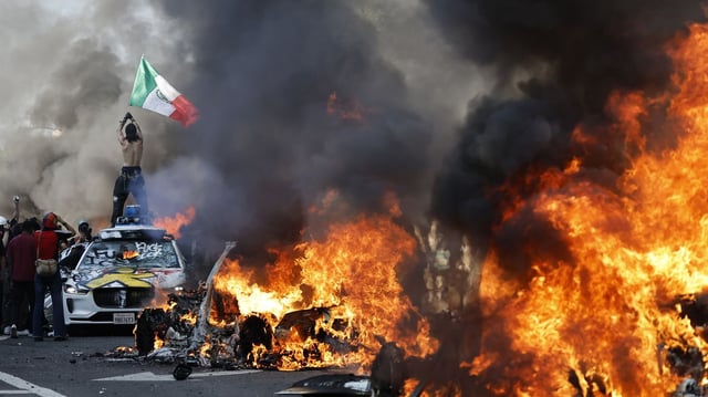 A protestor holds up a Mexican flag as burning cars line the street on June 8 in Los Angeles, California. Photo: Mario Tama/Getty Images
