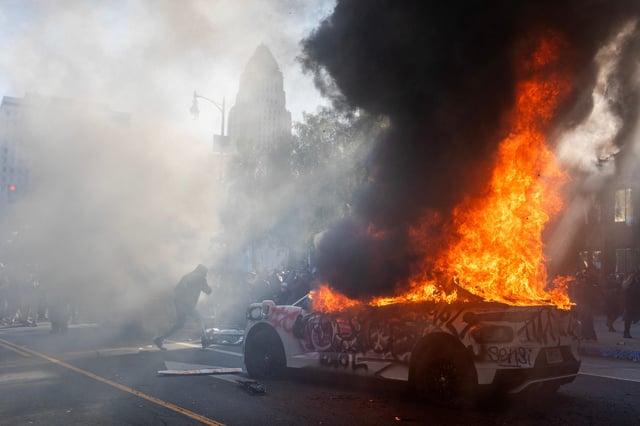 A Waymo vehicle burns as protesters clash with law enforcement in the streets surrounding the federal building during a protest following federal immigration operations in Los Angeles on June 8, 2025.