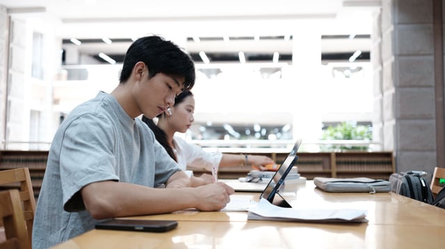 Students preparing for China’s rigorous gaokao college entrance exams, seen here using digital devices and study materials in a modern library setting. Amid fears of AI-enabled cheating, Chinese tech giants have suspended chatbot features while authorities deploy surveillance and network jammers to maintain exam integrity.