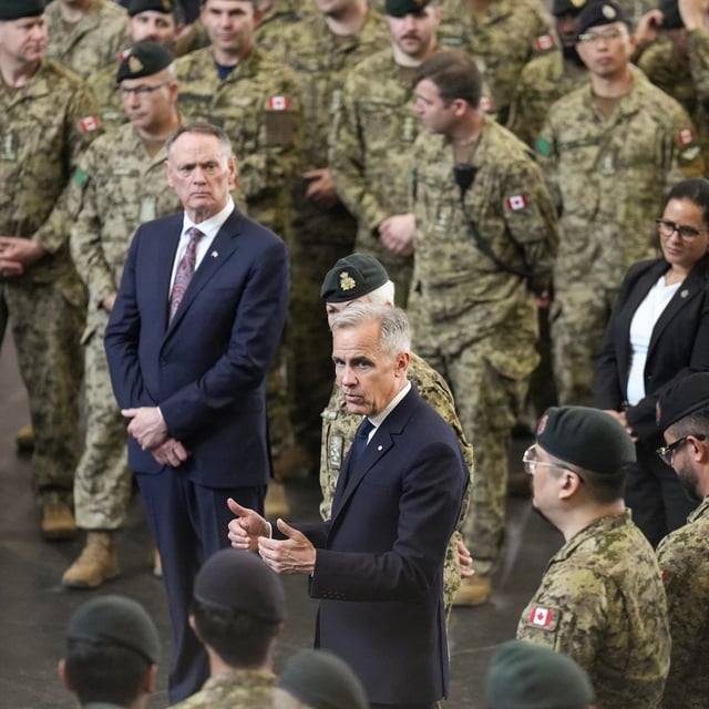 Prime Minister Mark Carney, centre, stands with Minister of National Defence David McGuinty, left, as he talks to service personnel following an announcement at Fort York Armoury in Toronto on June 9, 2025.
