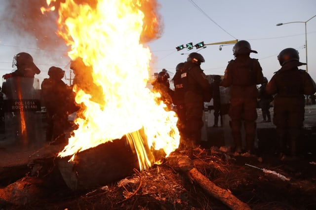 Des policiers boliviens près d'une barricade en feu montée par des partisans de l'ex-président Evo Morales, le 6 juin 2025 à Vinto