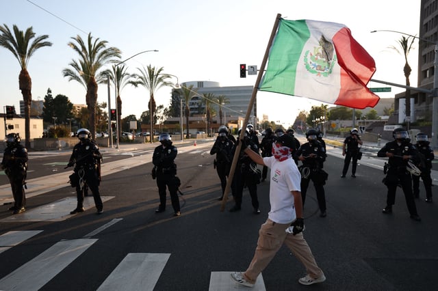 A person holds a Mexican flag outside the United States Citizenship and Immigration Services (USCIS) Santa Ana Field Office after reports of Immigration and Customs Enforcement (ICE) raids in Santa Ana, California, on June 9, 2025. The City of Santa Ana released a statement on Facebook acknowledging the ICE activity and the “fear and uncertainty” it would cause for some community members. President Donald Trump’s administration said on June 9 that it was sending 700 US Marines and thousands more National Guard troops to Los Angeles, sparking a furious response from California’s governor over the “deranged” deployment. (Photo by Patrick T. Fallon / AFP) (Photo by PATRICK T. FALLON/AFP via Getty Images)