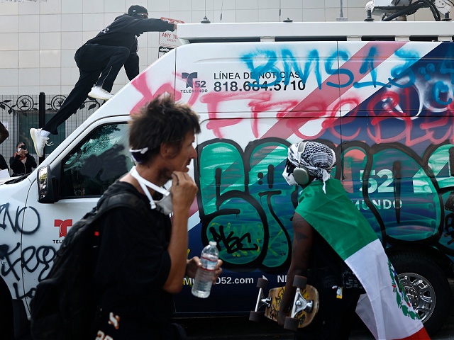 LOS ANGELES, CALIFORNIA - JUNE 09: (EDITORS NOTE: Image contains profanity) A person climbs on a vandalized news van as protests continue in Los Angeles following three days of clashes with police after a series of immigration raids on June 09, 2025 in Los Angeles, California. Tensions in the city remain high after the Trump administration called in the National Guard against the wishes of city leaders. (Photo by Mario Tama/Getty Images)