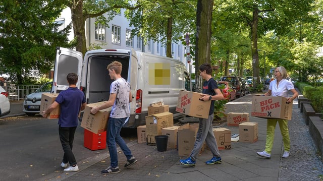 Menschen tragen Umzugkartons zu einem Kleintransporter.