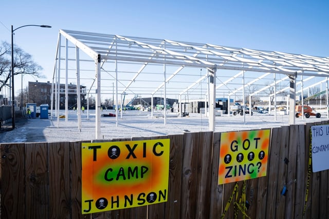 Signs proclaiming environmental hazards are posted on a fence as the tent encampment for migrants in constructed in the Brighton Park neighborhood, Nov. 29, 2023. (E. Jason Wambsgans/Chicago Tribune)