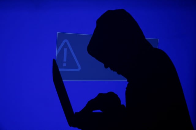 A hooded man holds a laptop computer as blue screen with an exclamation mark is projected on him in this illustration picture taken on May 13, 2017. REUTERS/Kacper Pempel/Illustration/File Photo