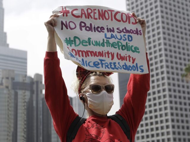 FILE - A demonstrator holds a sign in front of the downtown skyline during a protest to demand the defunding of the Los Angeles school district police outside of the school board headquarters Tuesday, June 23, 2020, in Los Angeles. The Los Angeles City Council has voted to slash the Police Department budget by $150 million, reducing the number of officers to a level not seen for more than a decade. The council approved the change Wednesday, July 1, 2020, dropping the number of officers to a little more than 9,700 by next summer. (AP Photo/Marcio Jose Sanchez, File)