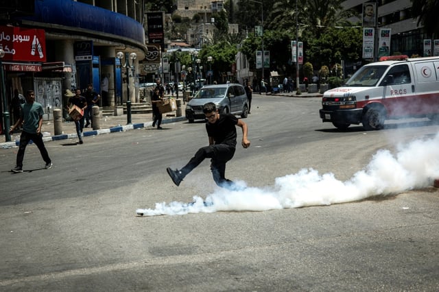 A Palestinian boy kicks a tear gas canister fired by Israeli forces during a military raid in Nablus