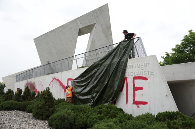 Workers from a cleanup crew spread a tarp to cover red paint spelling the words 'FEED ME' on the National Holocaust Monument in Ottawa on Monday, June 9, 2025. THE CANADIAN PRESS/Sean Kilpatrick