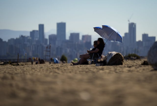 People sit under umbrellas at Locarno Beach in Vancouver on Wednesday, Aug. 16, 2023. THE CANADIAN PRESS/Darryl Dyck